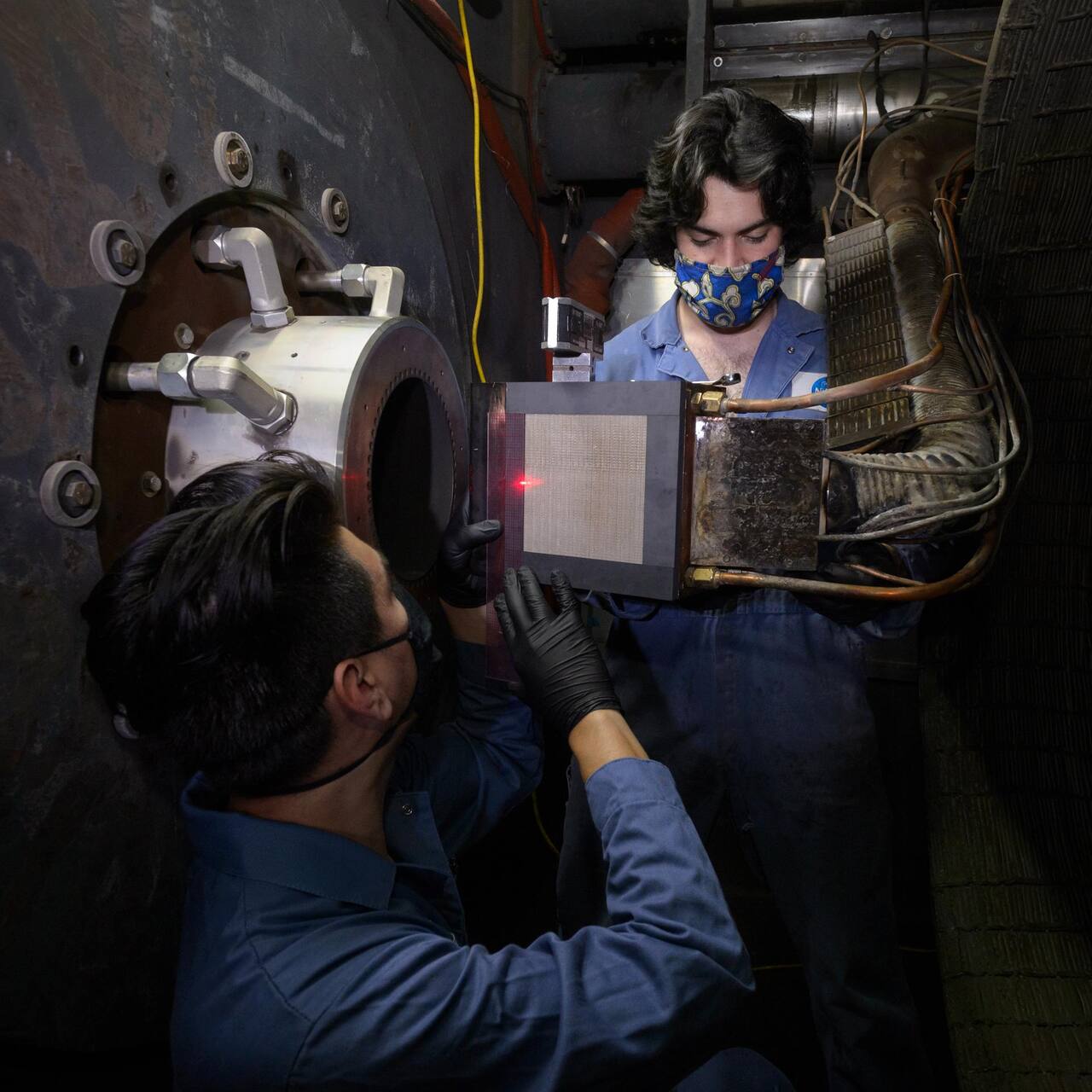 Engineering technicians verify alignment of an Orion heat shield test article in the Interaction Heating Facility test section, April 2021, for a combined IHF and LEAF-Lite radiant and convective heating test.