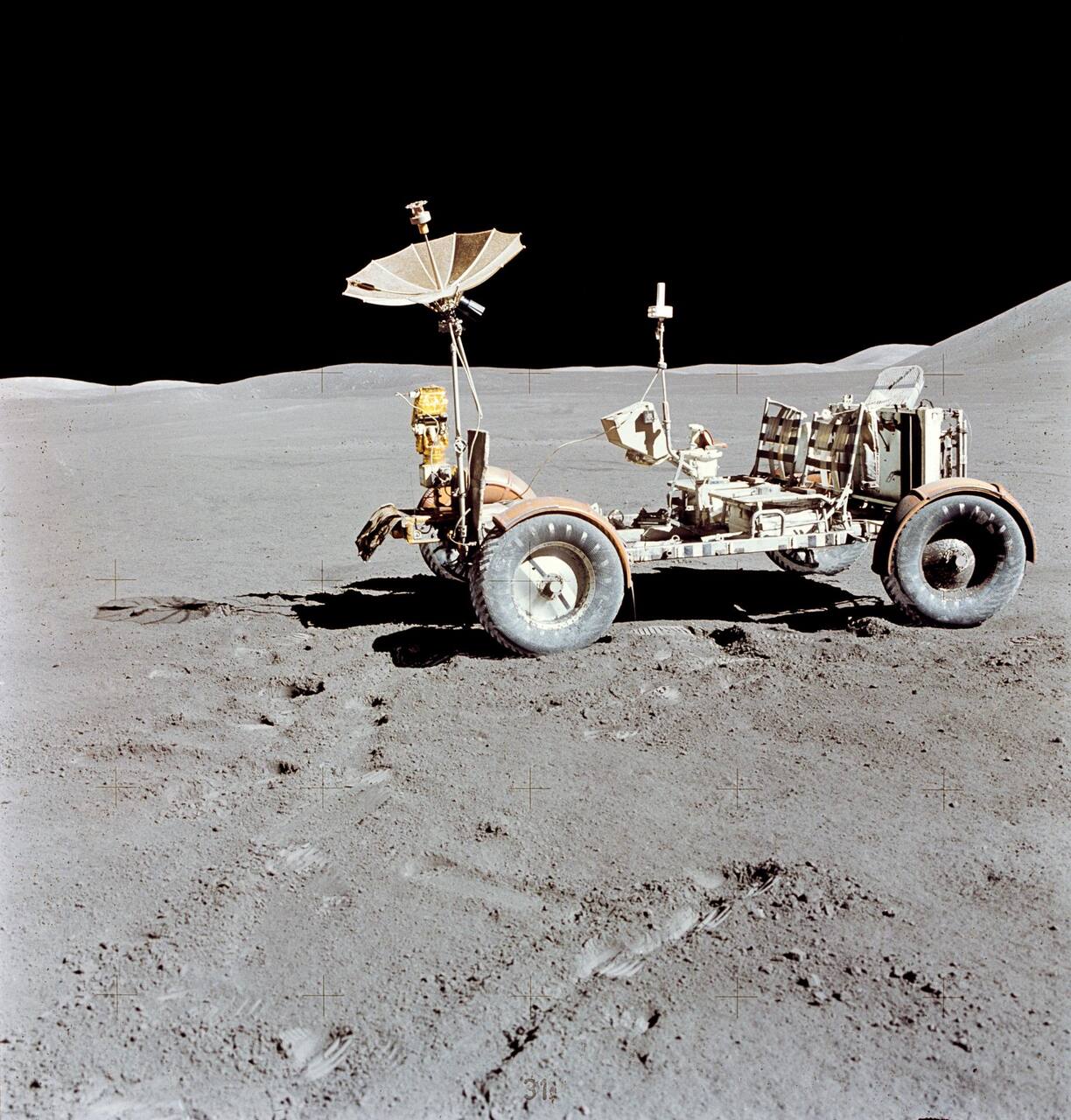 Apollo 15 Lunar Roving Vehicle parked alone at the Hadley-Apennine site during the third EVA, 31 July to 2 August 1971. The woven wire mesh wheels with partial chevron treads, the fenders whose loss on later missions coupled dust control to thermal control, and the deployed S-band high-gain antenna of the Lunar Communications Relay Unit are all visible
