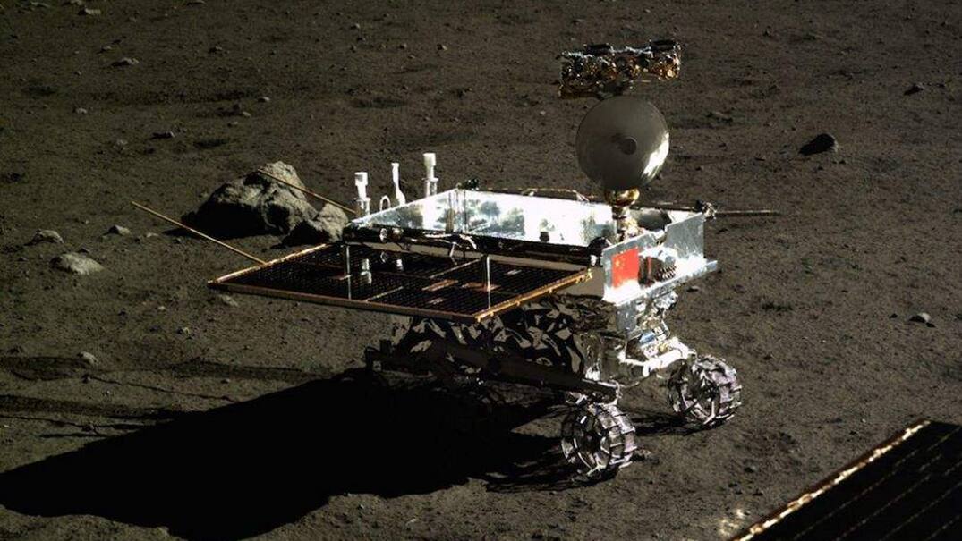 Yutu photographed from the Chang'e-3 lander in December 2013. Both solar wings are deployed horizontally, the lunar penetrating radar dipole antennas project fore and aft, the steerable dish sits on the mast, and three of the six grousered wheels are visible