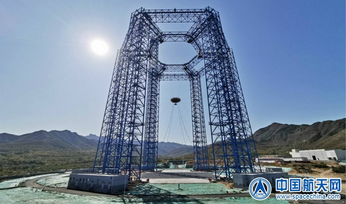 The Extraterrestrial Body Landing Comprehensive Test Field at Huailai, Hebei. Six steel towers carry the cable-parallel drive; the fast follow-up platform hangs at the center on the main hoist ropes with diagonal stay cables running down to ground drive units, above a prepared terrain field.