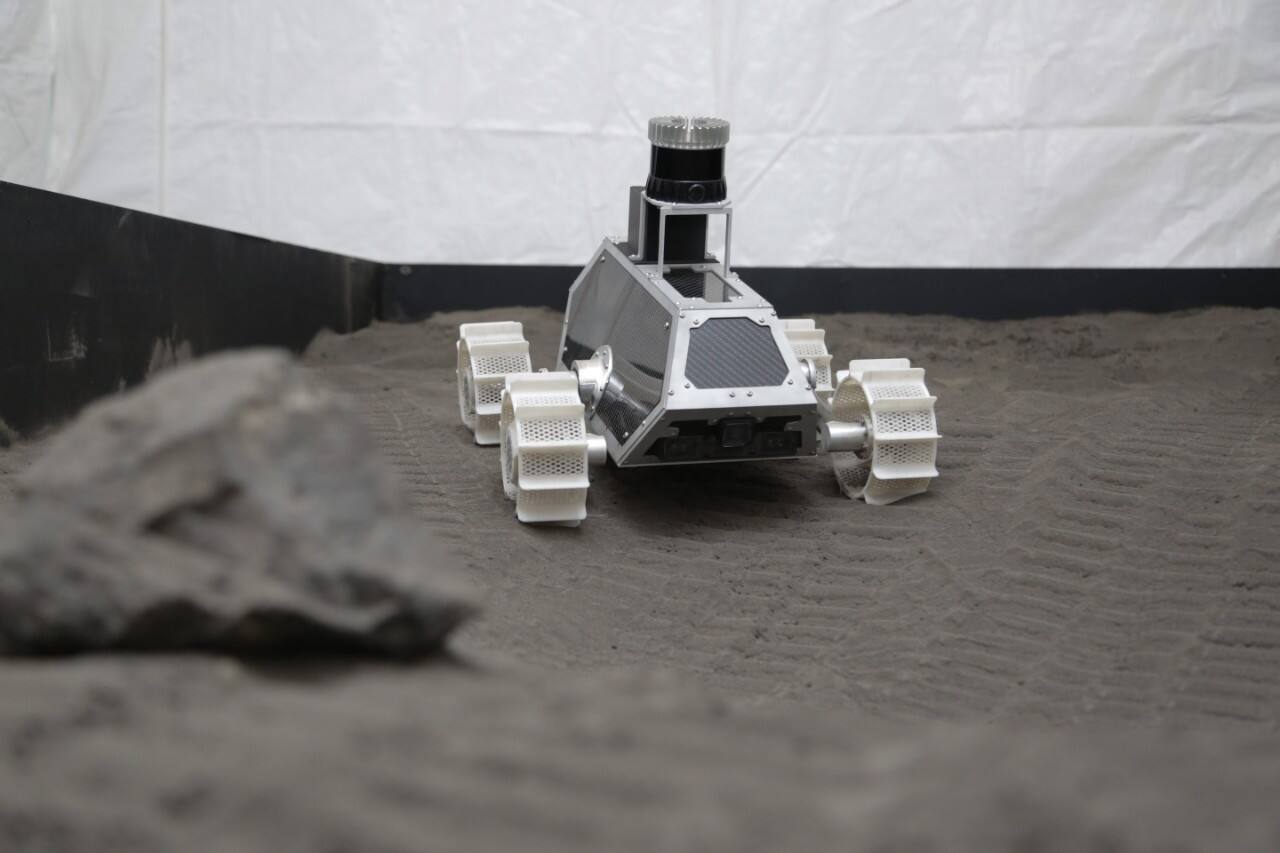 A rover in the original Colorado School of Mines lunar test bed at the Earth Mechanics Institute. The bed is milled Merriam Crater basaltic cinder over coarser 8 mm cinder, with loose rock fragments laid on the surface.