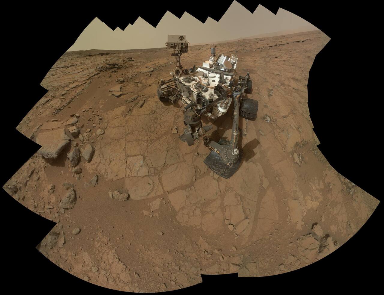 Curiosity self-portrait taken by the MAHLI camera on the arm turret at the John Klein outcrop, February 2013, the site of the first rock drilling. The mosaic shows the six 0.5 m wheels on rocker-bogie suspension, the MMRTG projecting from the rear deck, and the mast carrying ChemCam and the Mastcams