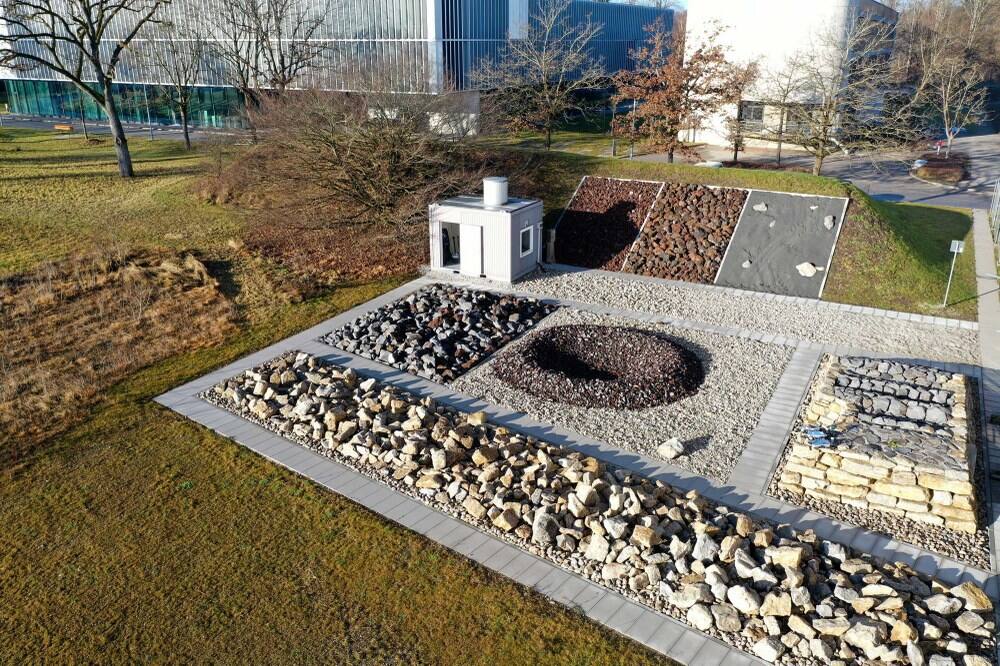 The planetary test field at DLR Oberpfaffenhofen from above, with the graded beds of basaltic gravel, coarse blocks and light limestone laid out in adjacent panels beside the slope panel and the control cabin.