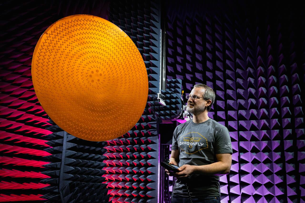 The Dragonfly high-gain antenna under test in an anechoic chamber, the pyramidal absorber lining the walls behind it. This dish is the whole of the mission's downlink: Dragonfly carries no relay orbiter and talks direct to Earth in X-band only, which is why the mission is confined to latitudes from which Earth is visible from the surface. On the vehicle the antenna stows flat behind an aerodynamic fairing ahead of its gimbal, so that it does not disturb rotor flight