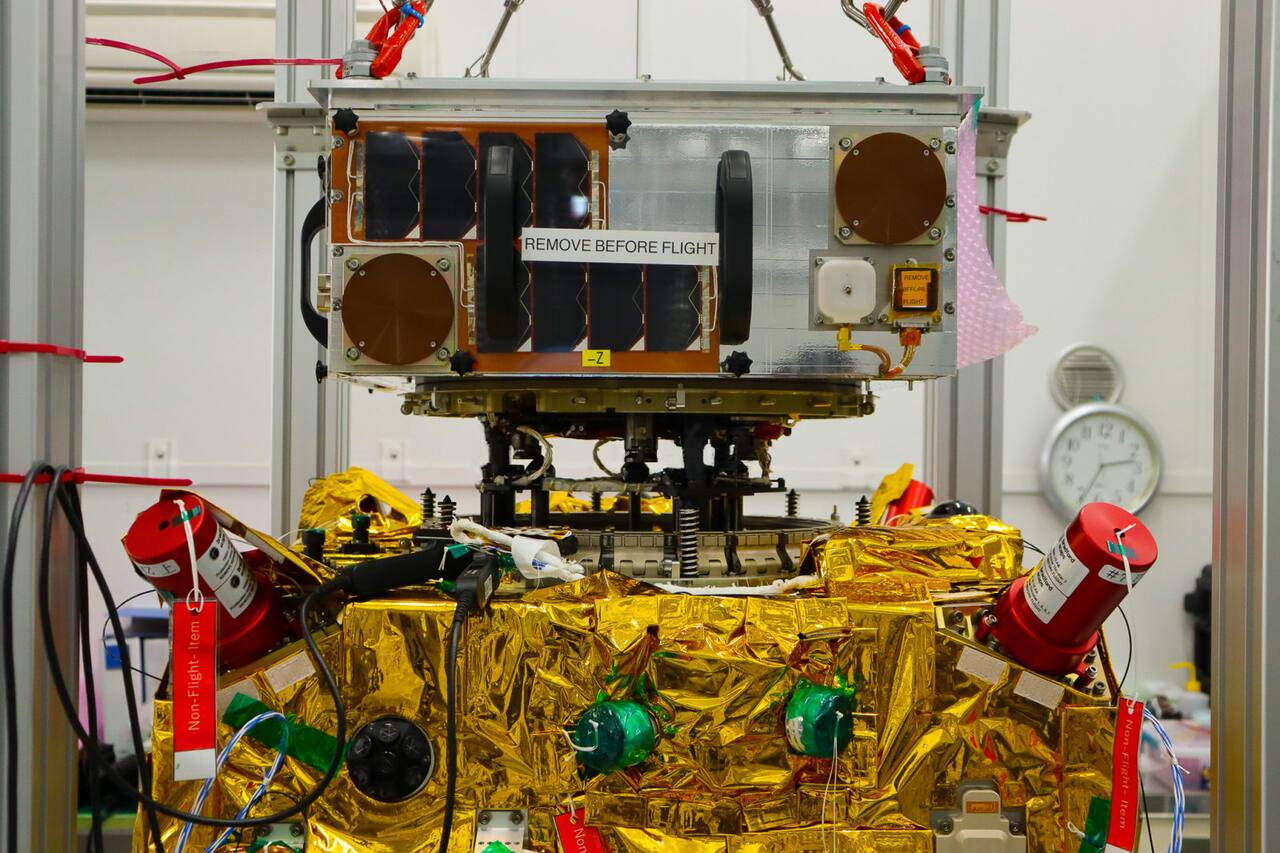 ELSA-d during integration. The client, above, carries body-mounted solar cells and the ferromagnetic docking plate on its underside; the servicer below is wrapped in multi-layer insulation with red non-flight covers on two thruster clusters. The separation springs and the capture mechanism stand between them.