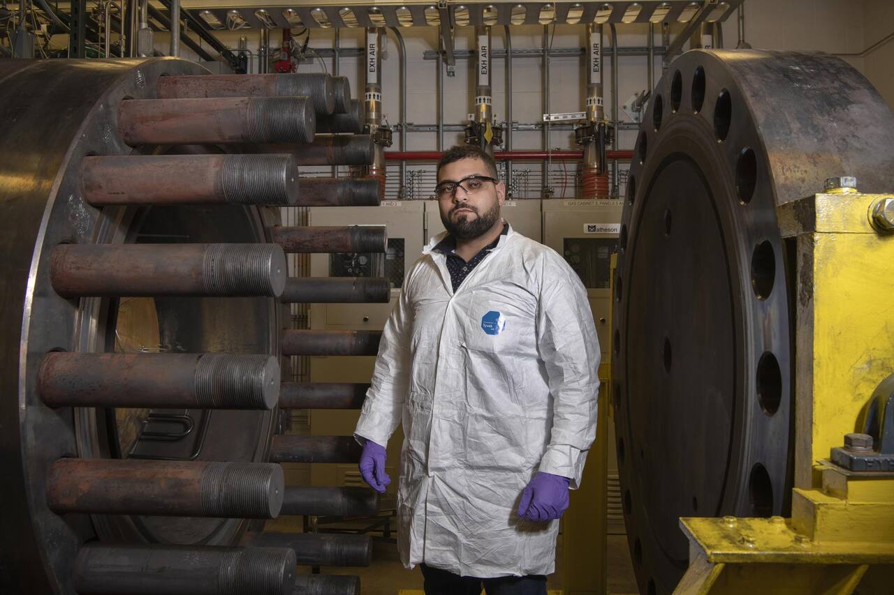The GEER pressure vessel in its test cell at NASA Glenn, March 2022: the insulated horizontal vessel with its bolted end closure at left, the gas mixing lines entering at the near end, and a technician at the working level for scale.