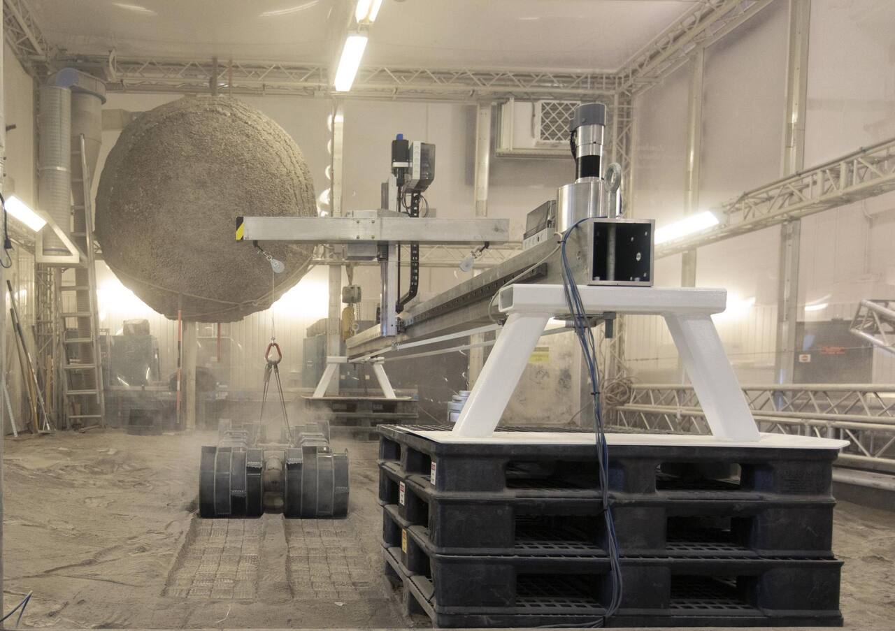 RASSOR excavating BP-1 in the main regolith bin on 5 June 2019, slung from the overhead beam above the bin, with both counter-rotating bucket drums at the bed surface.