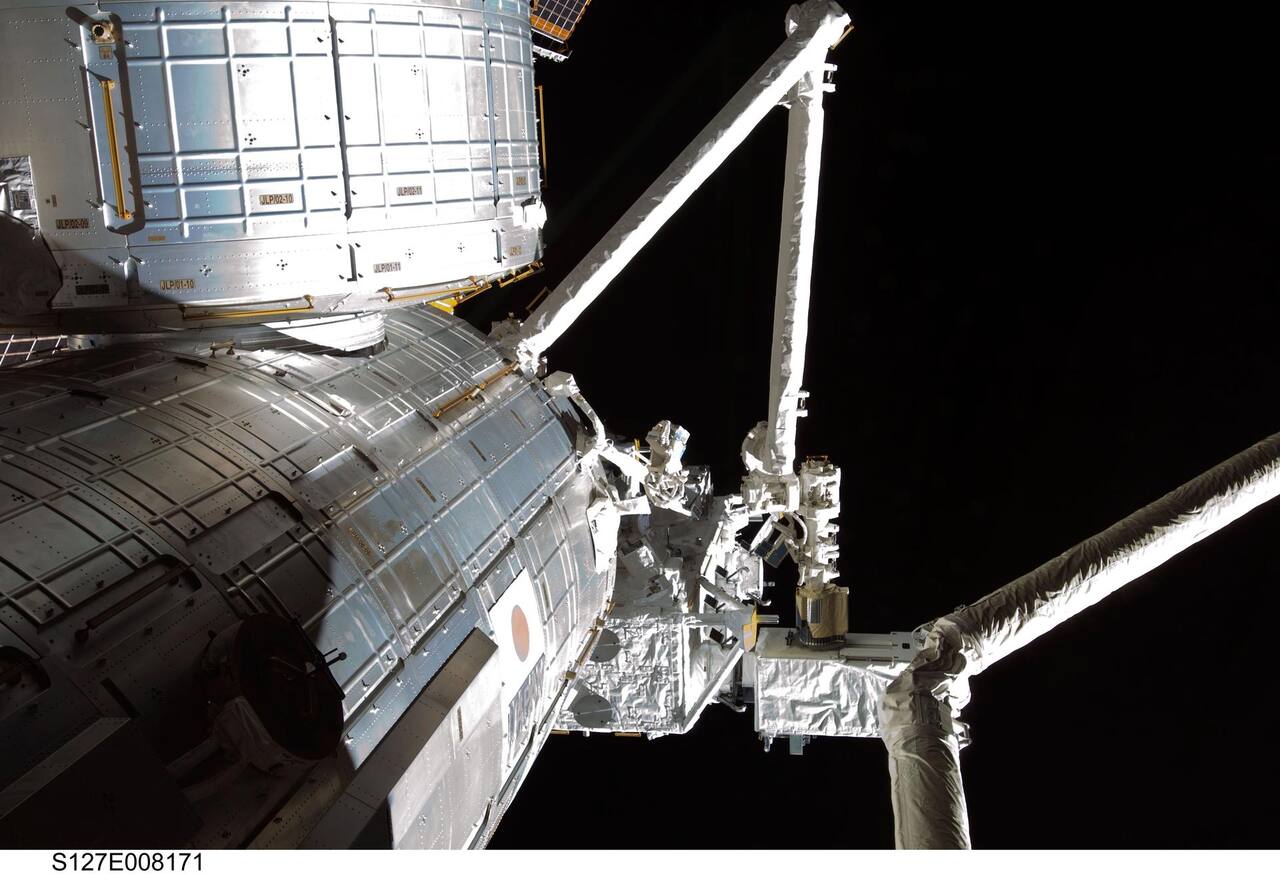 The JEMRMS main arm, upper right, holding the Interorbital Communication System payload after unberthing it from the Kibo Exposed Facility during STS-127 on 23 July 2009. The two CFRP booms and the wrist joint cluster stand against the Kibo pressurized module; the thicker boom entering from the lower right is Canadarm2.