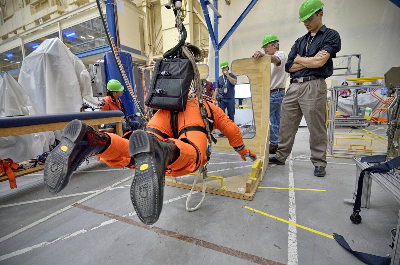Astronaut Rex Walheim using the Active Response Gravity Offload System to perform early evaluations of the Orion Crew Survival System suit in Building 9 at NASA JSC, 5 June 2012.