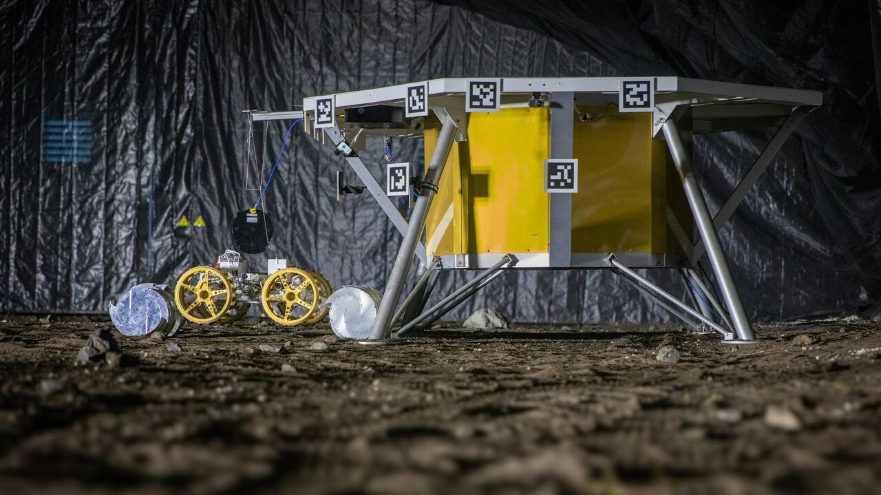 The KSC autonomy test site on 30 August 2024, during the five-day TRL 5 mission demonstration. A single stadium fixture at one end throws the long, hard-edged shadows the site is built to produce; the mock lander carries the fiducial targets used for pose estimation, and a small rover stands beside its leg.