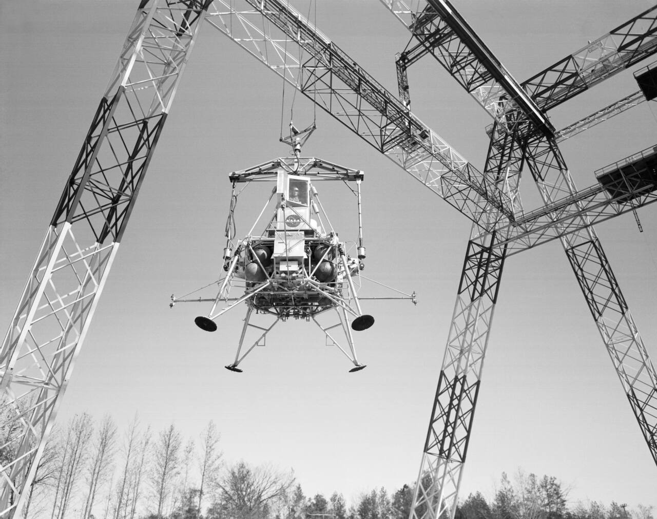 A Lunar Excursion Module Simulator descending under the Lunar Landing Research Facility gantry, 15 November 1967, with the vertical suspension cable and the movable bridge above it.