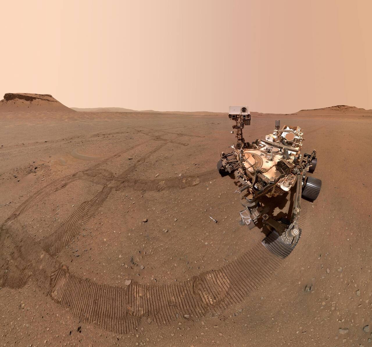 Perseverance photographed by the WATSON camera on its arm turret at the Three Forks sample depot in Jezero crater on sol 684, 22 January 2023, a mosaic of 59 frames. One of the ten deposited sample tubes lies on the ground in front of the rover; the 52.5 cm wheels, the MMRTG at the rear and the mast head carrying Mastcam-Z and SuperCam are all visible