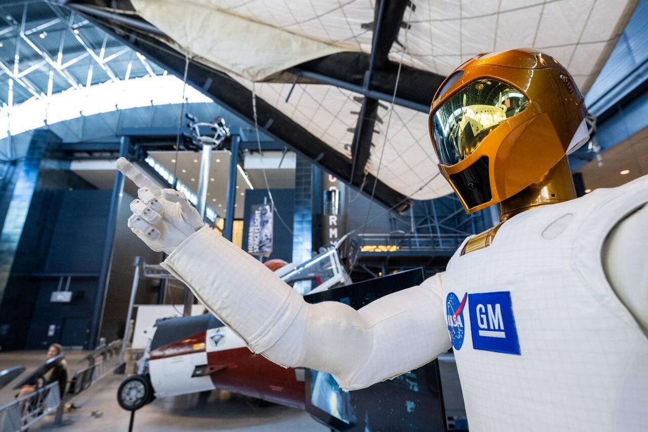 Robonaut 2 on display at the National Air and Space Museum Udvar-Hazy Center, 24 October 2024, carrying both the NASA and General Motors marks of the joint development. The right arm is extended through the five series elastic joints that run from shoulder to wrist, and the hand shows the twelve degrees of freedom per hand that let R2 work crew tools and soft goods; the two-degree-of-freedom wrist sits under the fabric cuff. The gold head carries the three-degree-of-freedom pan and tilt with the stereo cameras behind the visor
