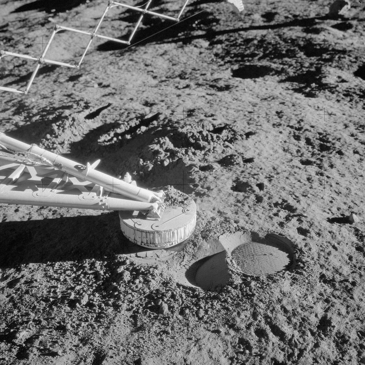 Close-up of the Surveyor 3 surface sampler scoop and an adjacent footpad, photographed by the Apollo 12 crew on 20 November 1969, two and a half years after the sampler last operated. The drum-shaped scoop with its hinged door is the working end of the arm, and the imprint beside it was made when Surveyor 3 bounced on landing